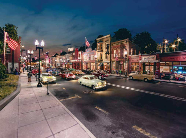 Scenic nighttime view of a vintage-style street with classic cars, illuminated shops, and American flags.