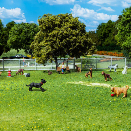 Miniature HO scale figures of cats and dogs playing in a park with trees and a fence, ideal for model layouts.