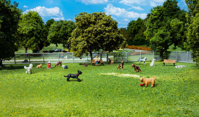 Miniature HO scale figures of cats and dogs playing in a park with trees and a fence, ideal for model layouts.