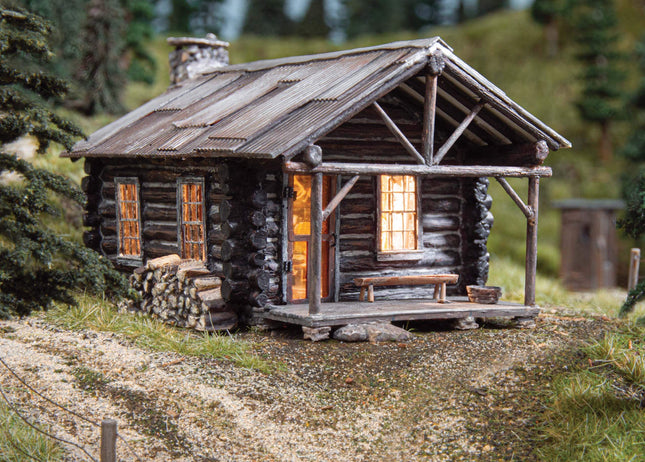 O Scale Cozy Cabin by Woodland Scenics with glowing interior and rustic exterior in a rural setting.