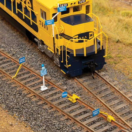 HO scale model train with blue safety flags indicating worker presence near tracks.